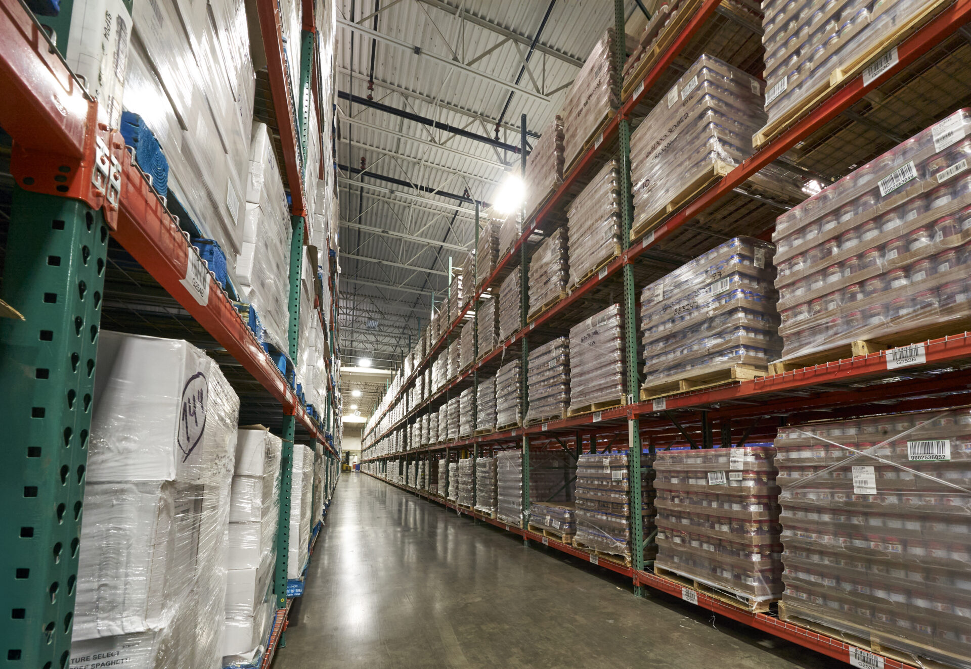 Pallets with multiple brands of peanut butter are shelved on large industrial racking.
